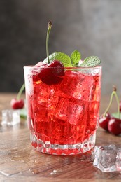 Photo of Tasty cherry soda with ice cubes, berries and mint in glass on wooden table, closeup