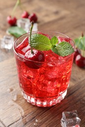 Photo of Tasty cherry soda with ice cubes, berries and mint in glass on wooden table, closeup