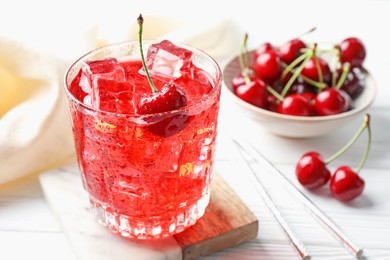 Photo of Tasty cherry soda with ice cubes and berries in glass on white wooden table, closeup
