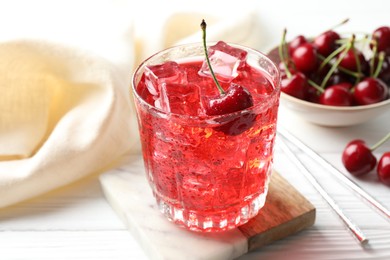 Photo of Tasty cherry soda with ice cubes and berries in glass on white wooden table, closeup