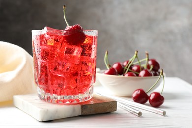 Photo of Tasty cherry soda with ice cubes and berries in glass on white wooden table, closeup