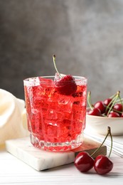 Photo of Tasty cherry soda with ice cubes and berries in glass on white wooden table, closeup