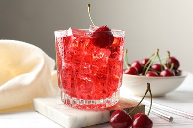 Photo of Tasty cherry soda with ice cubes and berries in glass on white wooden table, closeup