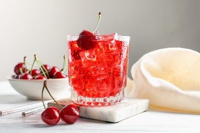 Photo of Tasty cherry soda with ice cubes and berries in glass on white wooden table, closeup