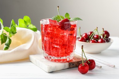 Photo of Tasty cherry soda with ice cubes, berries and mint in glass on white wooden table, closeup