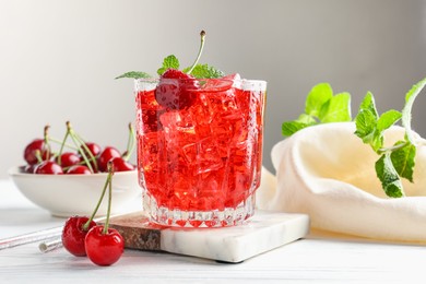 Photo of Tasty cherry soda with ice cubes, berries and mint in glass on white wooden table, closeup