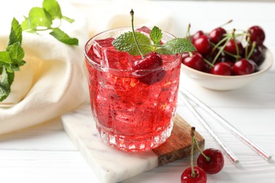 Photo of Tasty cherry soda with ice cubes, berries and mint in glass on white wooden table, closeup