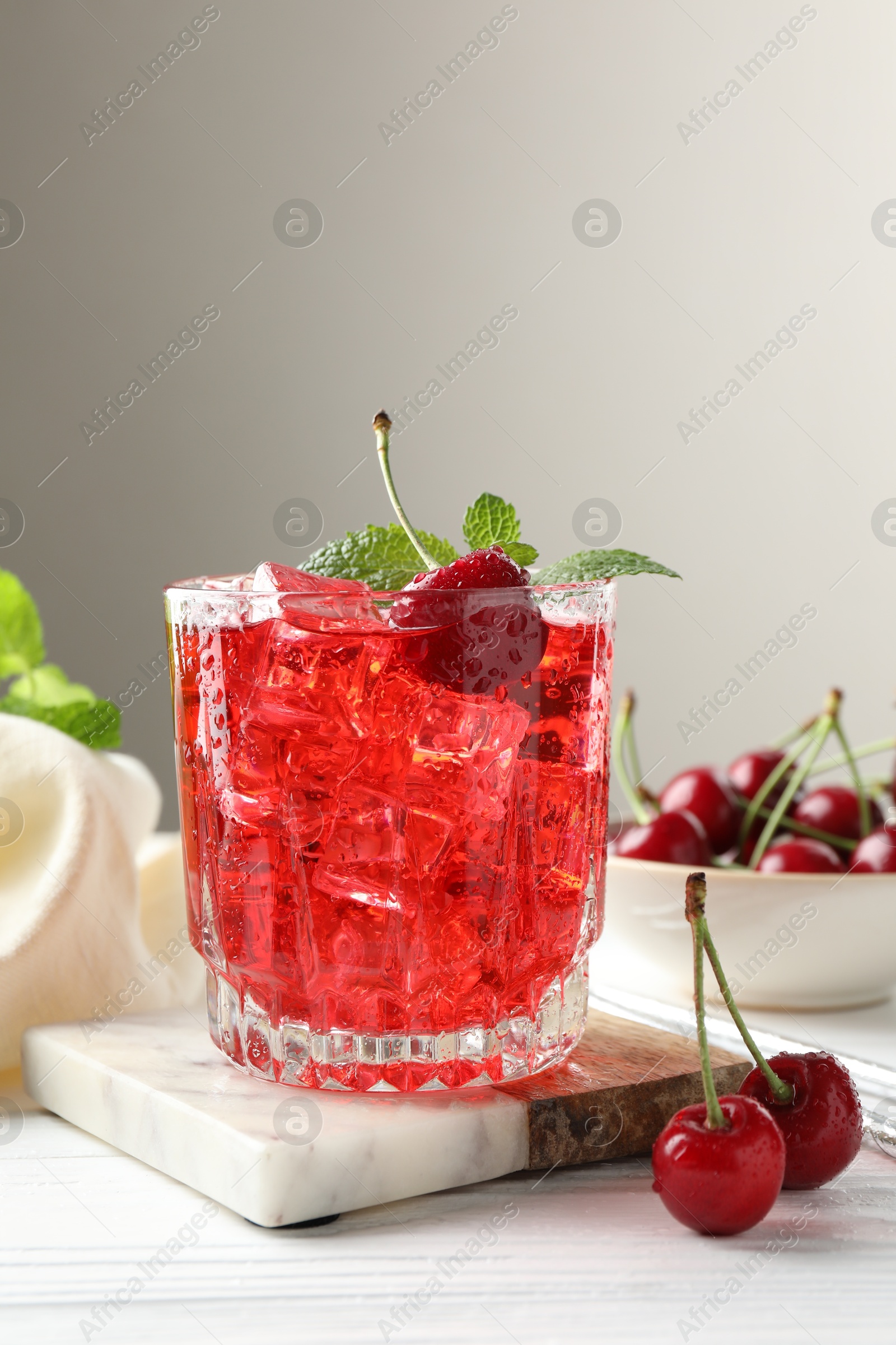 Tasty cherry soda with ice cubes, berries and mint in glass on white wooden table, closeup Photo of Tasty cherry soda with ice cubes, berries and mint in glass on white wooden table, closeup