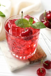 Photo of Tasty cherry soda with ice cubes, berries and mint in glass on white wooden table, closeup