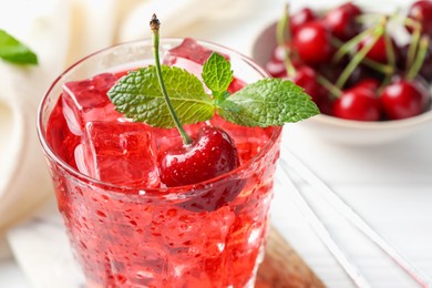 Photo of Tasty cherry soda with ice cubes, berries and mint in glass on white wooden table, closeup