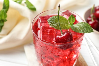 Photo of Tasty cherry soda with ice cubes, berries and mint in glass on white wooden table, closeup