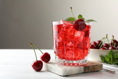Photo of Tasty cherry soda with ice cubes, berries and mint in glass on white wooden table, closeup. Space for text