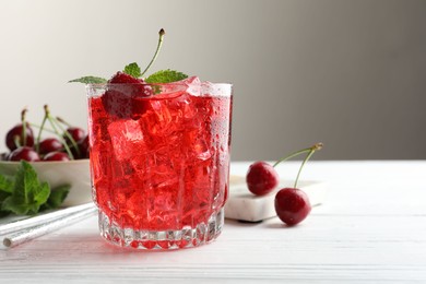 Photo of Tasty cherry soda with ice cubes, berries and mint in glass on white wooden table, closeup. Space for text