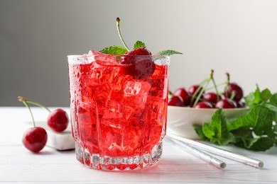 Photo of Tasty cherry soda with ice cubes, berries and mint in glass on white wooden table, closeup