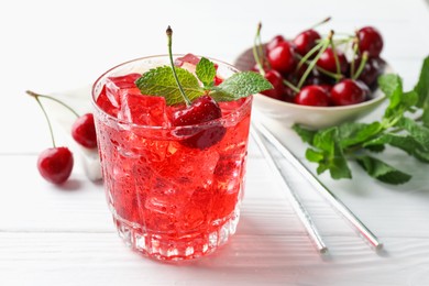 Photo of Tasty cherry soda with ice cubes, berries and mint in glass on white wooden table, closeup