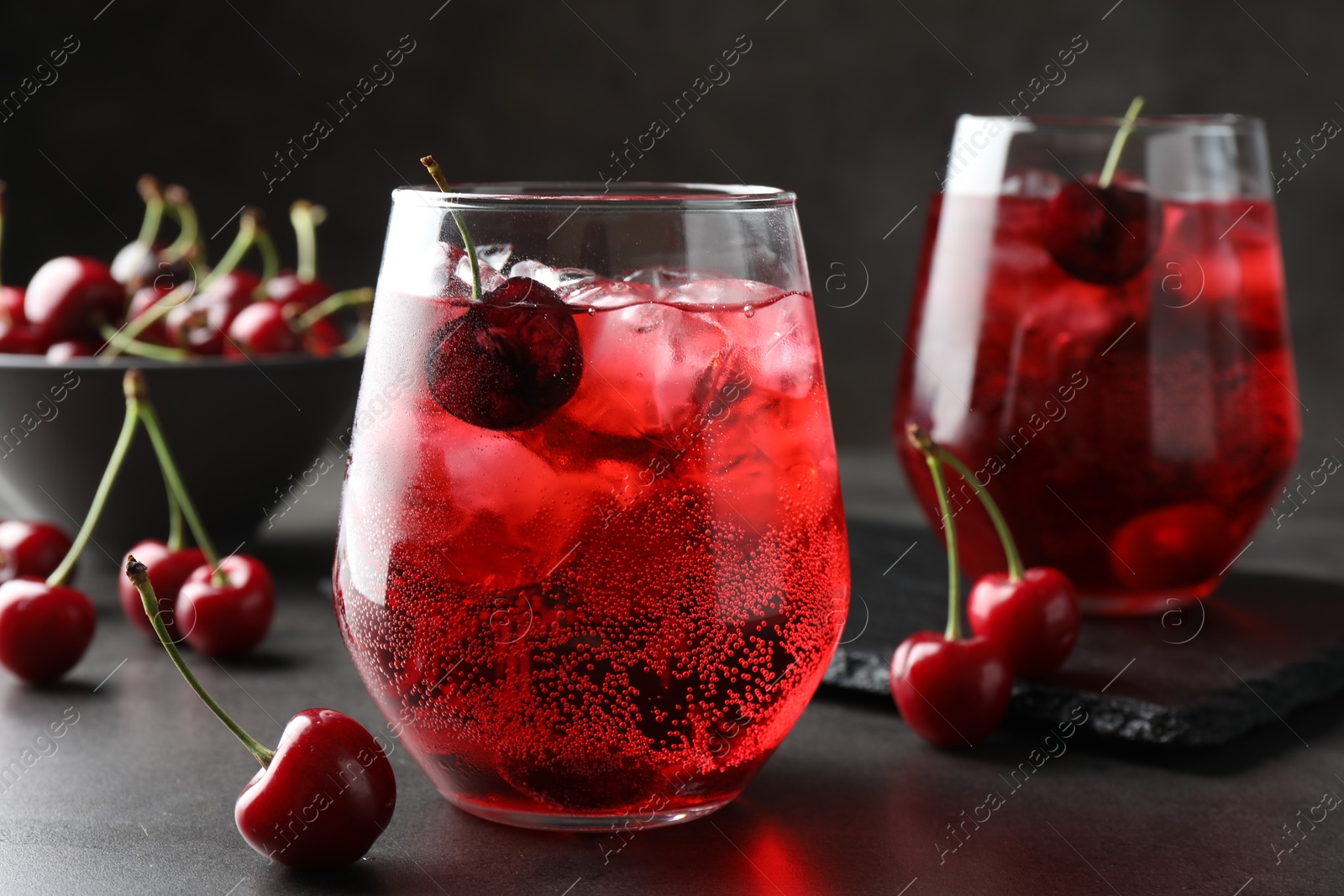 Tasty cherry soda with ice cubes and berries in glasses on grey table, closeup Photo of Tasty cherry soda with ice cubes and berries in glasses on grey table, closeup