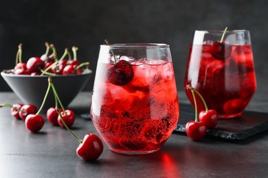Photo of Tasty cherry soda with ice cubes and berries in glasses on grey table, closeup