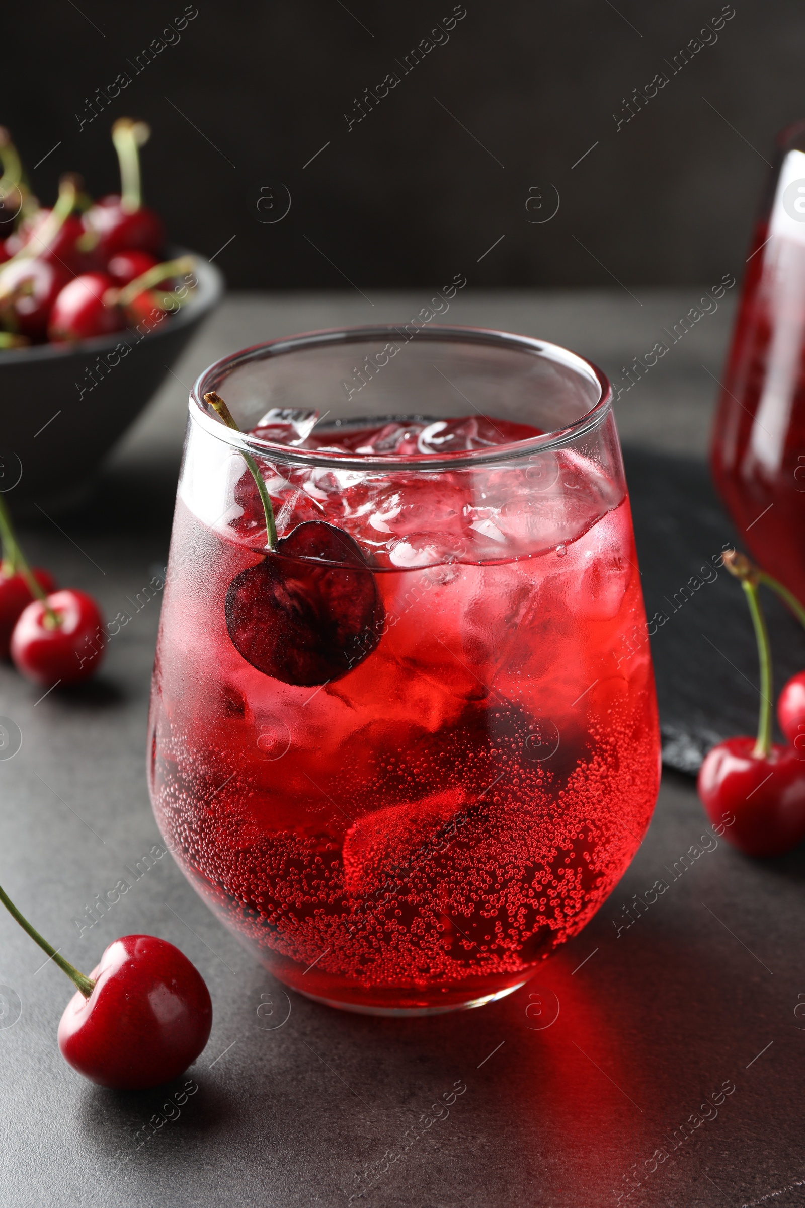 Tasty cherry soda with ice cubes and berries in glass on grey table, closeup Photo of Tasty cherry soda with ice cubes and berries in glass on grey table, closeup