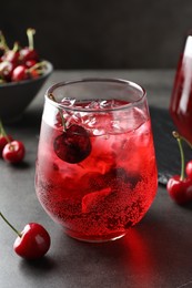 Photo of Tasty cherry soda with ice cubes and berries in glass on grey table, closeup