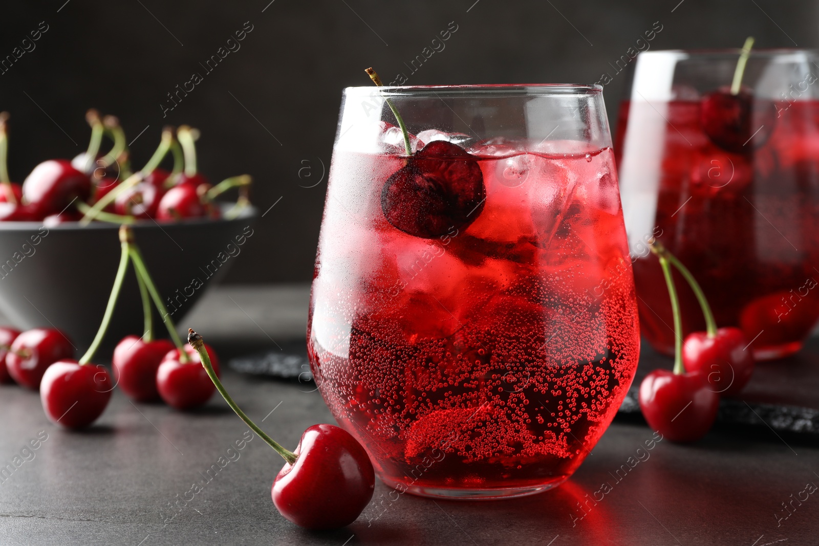 Tasty cherry soda with ice cubes and berries in glasses on grey table, closeup Photo of Tasty cherry soda with ice cubes and berries in glasses on grey table, closeup