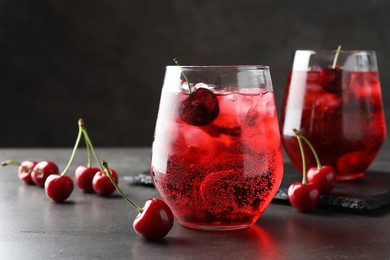 Photo of Tasty cherry soda with ice cubes and berries in glasses on grey table, closeup