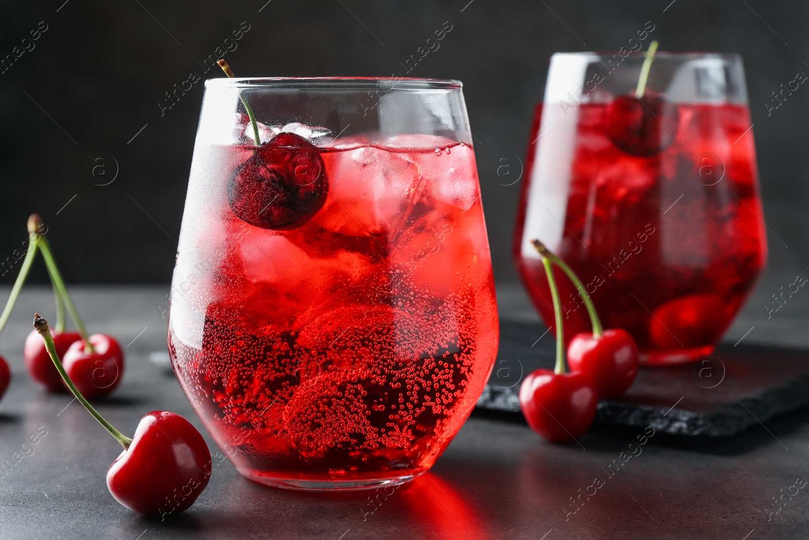 Tasty cherry soda with ice cubes and berries in glasses on grey table, closeup Photo of Tasty cherry soda with ice cubes and berries in glasses on grey table, closeup