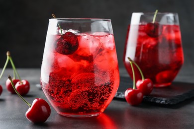 Photo of Tasty cherry soda with ice cubes and berries in glasses on grey table, closeup