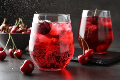 Photo of Tasty cherry soda with ice cubes and berries in glasses on grey table, closeup