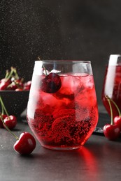 Photo of Tasty cherry soda with ice cubes and berries in glasses on grey table, closeup