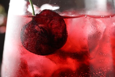 Photo of Tasty cherry soda with ice cubes and berry in glass, closeup