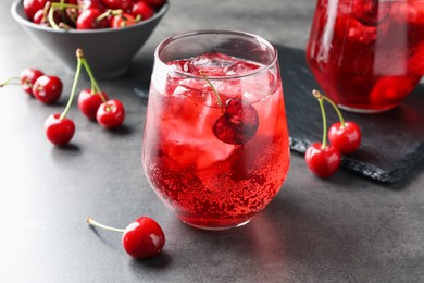 Photo of Tasty cherry soda with ice cubes and berries in glasses on grey table, closeup