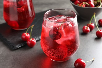 Photo of Tasty cherry soda with ice cubes and berries in glasses on grey table, closeup