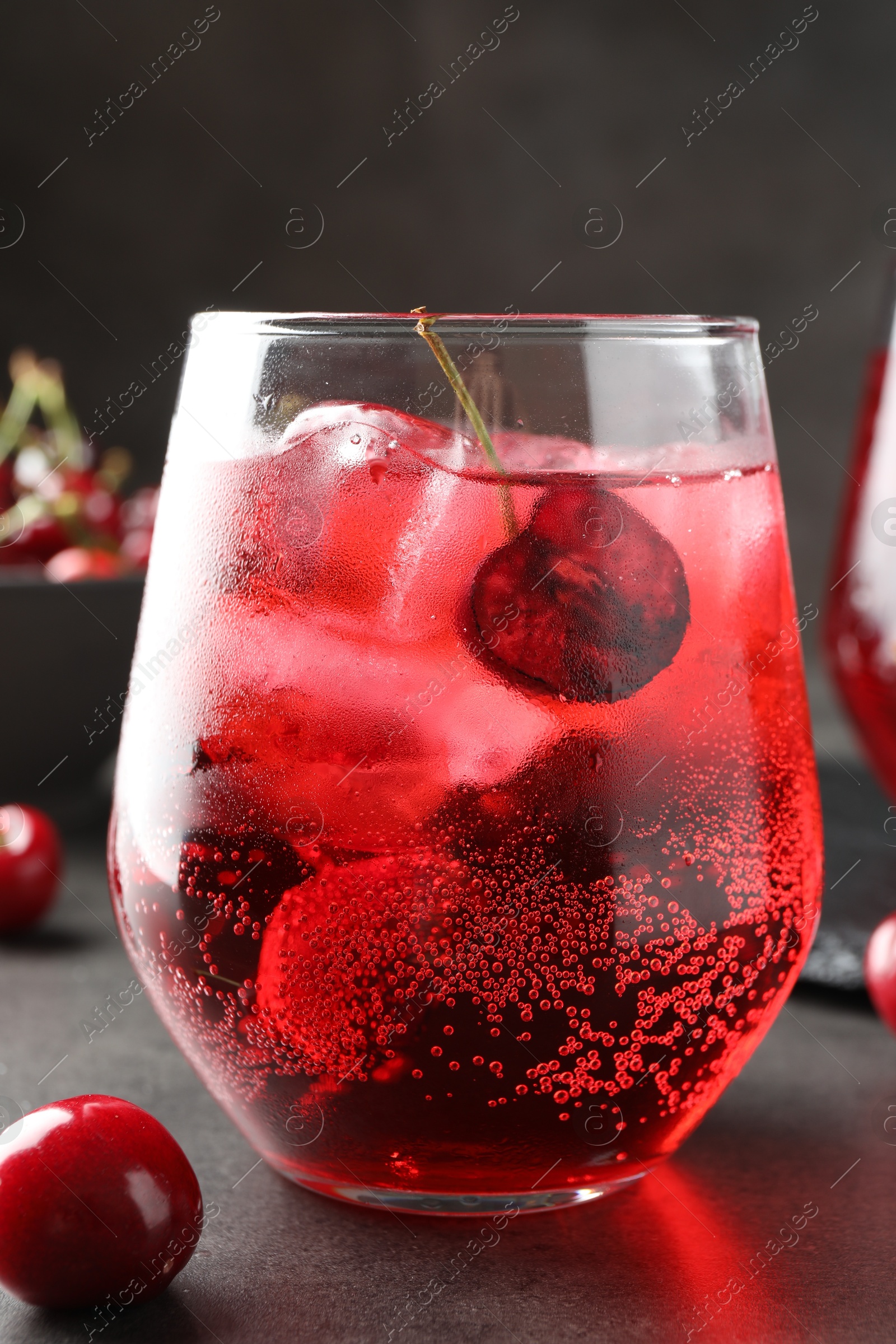 Tasty cherry soda with ice cubes and berries in glass on grey table, closeup Photo of Tasty cherry soda with ice cubes and berries in glass on grey table, closeup