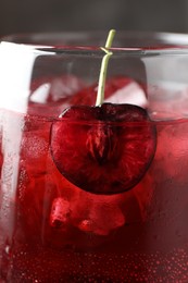 Photo of Tasty cherry soda with ice cubes and berry in glass on grey background, closeup