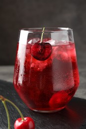 Photo of Tasty cherry soda with ice cubes and berries in glass on grey table, closeup