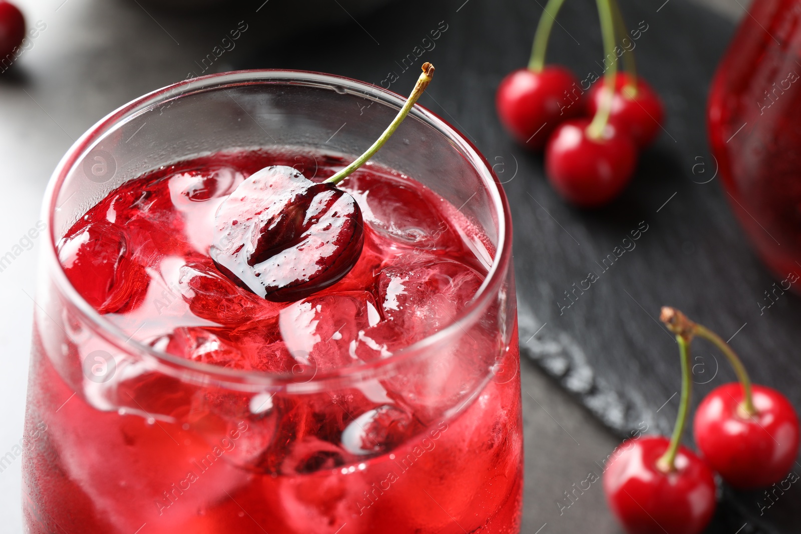 Tasty cherry soda with ice cubes and berries in glass on grey table, closeup Photo of Tasty cherry soda with ice cubes and berries in glass on grey table, closeup