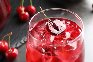 Photo of Tasty cherry soda with ice cubes and berries in glass on grey table, closeup