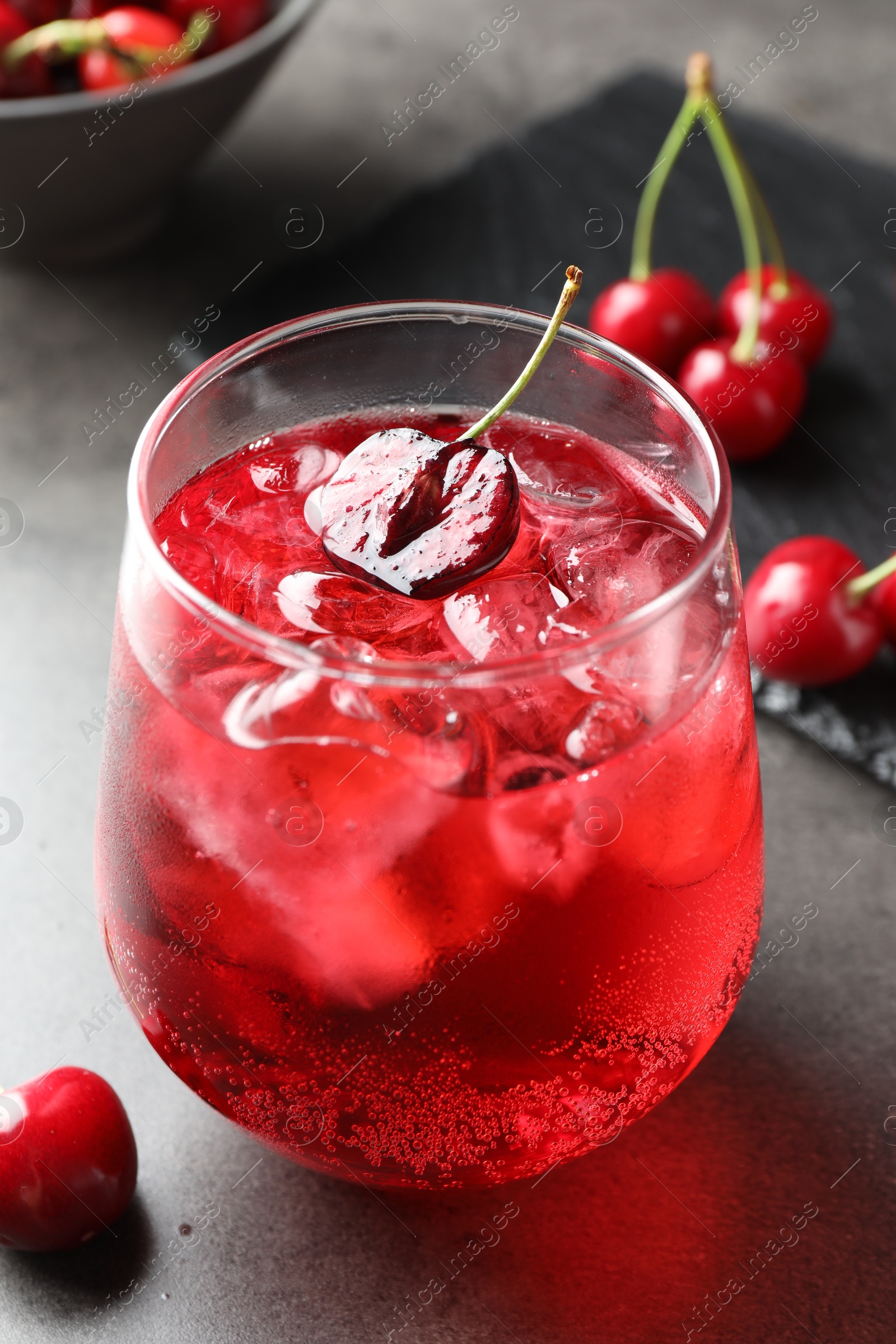 Tasty cherry soda with ice cubes and berries in glass on grey table, closeup Photo of Tasty cherry soda with ice cubes and berries in glass on grey table, closeup
