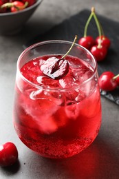 Photo of Tasty cherry soda with ice cubes and berries in glass on grey table, closeup
