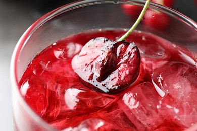 Photo of Tasty cherry soda with ice cubes and berry in glass on grey table, closeup