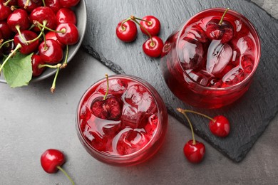 Photo of Tasty cherry soda with ice cubes and berries in glasses on grey table, flat lay