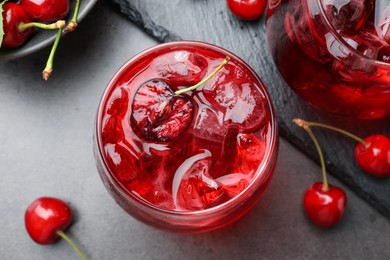 Photo of Tasty cherry soda with ice cubes and berries in glasses on grey table, flat lay