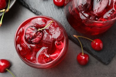 Photo of Tasty cherry soda with ice cubes and berries in glasses on grey table, flat lay