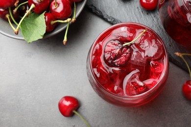 Photo of Tasty cherry soda with ice cubes and berries in glasses on grey table, flat lay