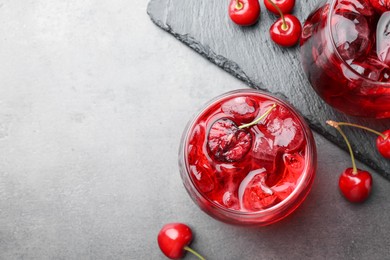 Photo of Tasty cherry soda with ice cubes and berries in glasses on grey table, flat lay