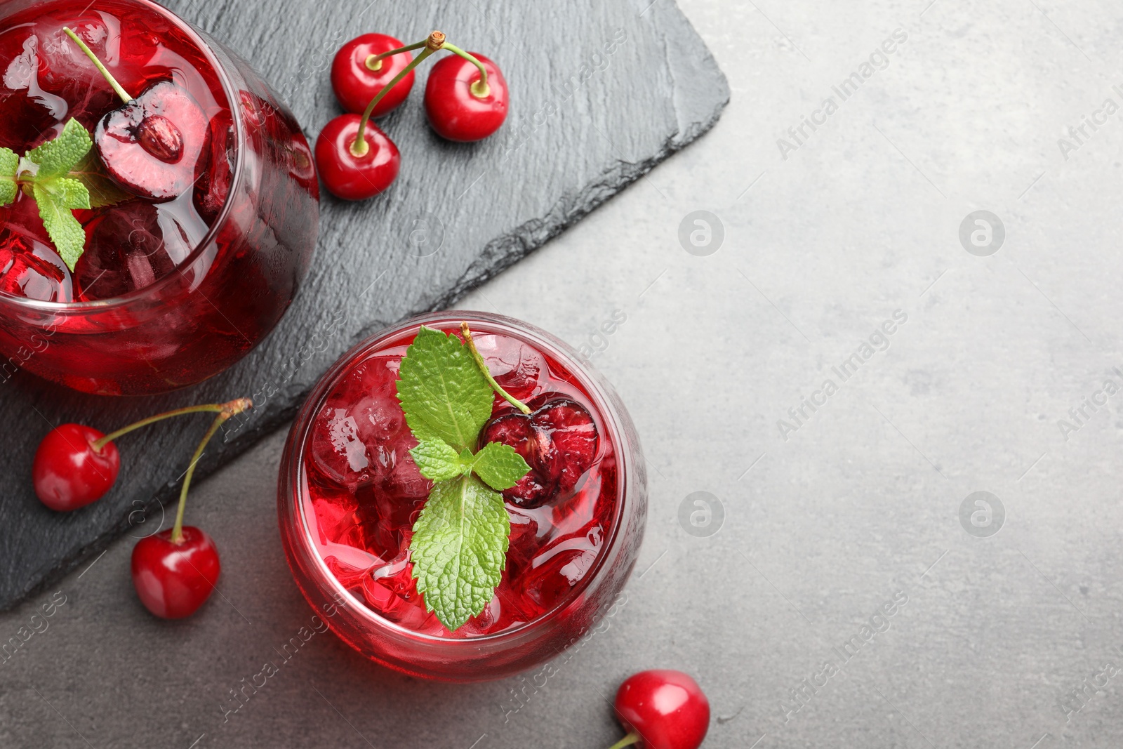 Tasty cherry soda with ice cubes, berries and mint in glasses on grey table, flat lay. Space for text Photo of Tasty cherry soda with ice cubes, berries and mint in glasses on grey table, flat lay. Space for text