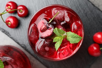 Photo of Tasty cherry soda with ice cubes, berries and mint in glasses on grey table, flat lay