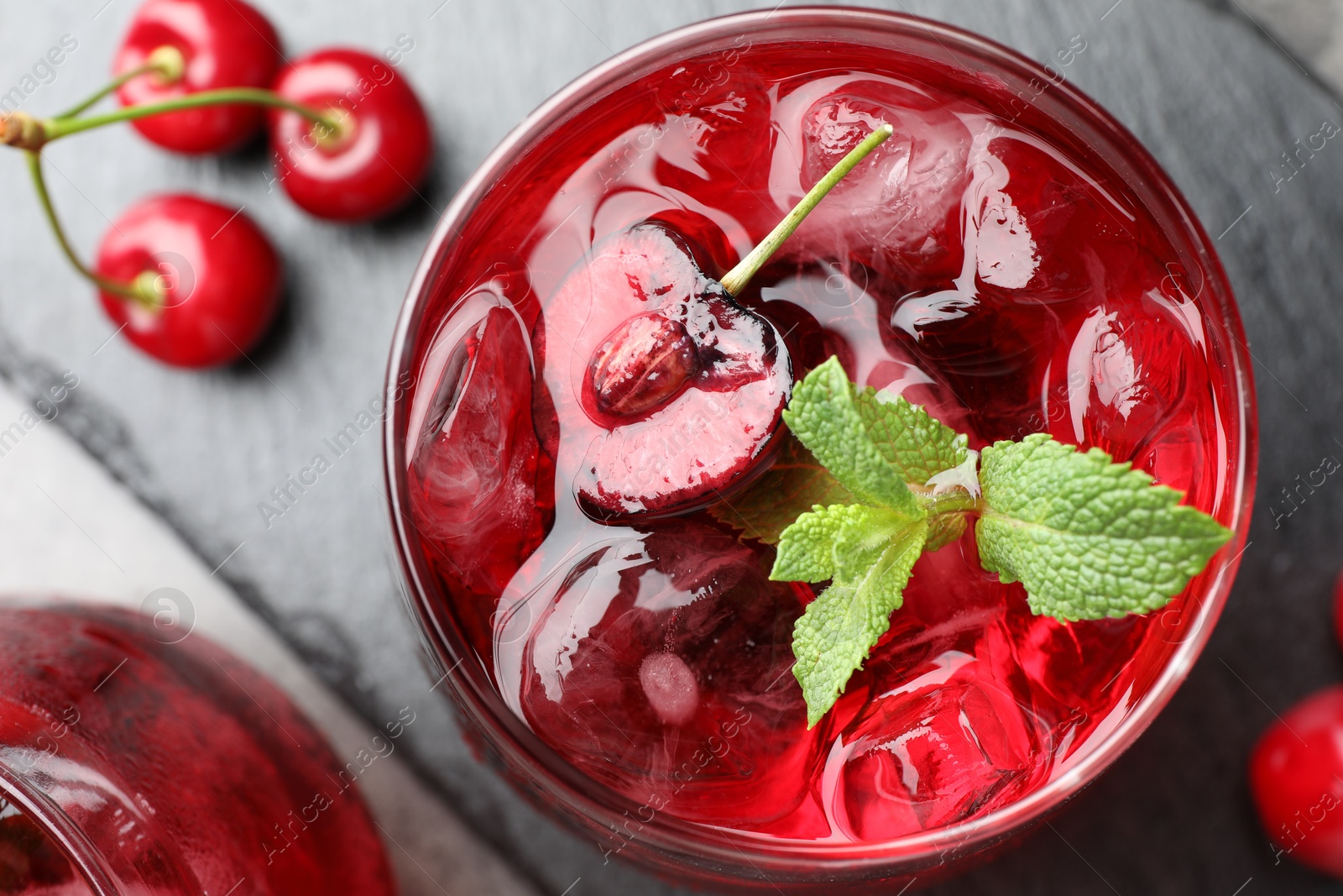 Tasty cherry soda with ice cubes, berries and mint in glasses on grey table, flat lay Photo of Tasty cherry soda with ice cubes, berries and mint in glasses on grey table, flat lay