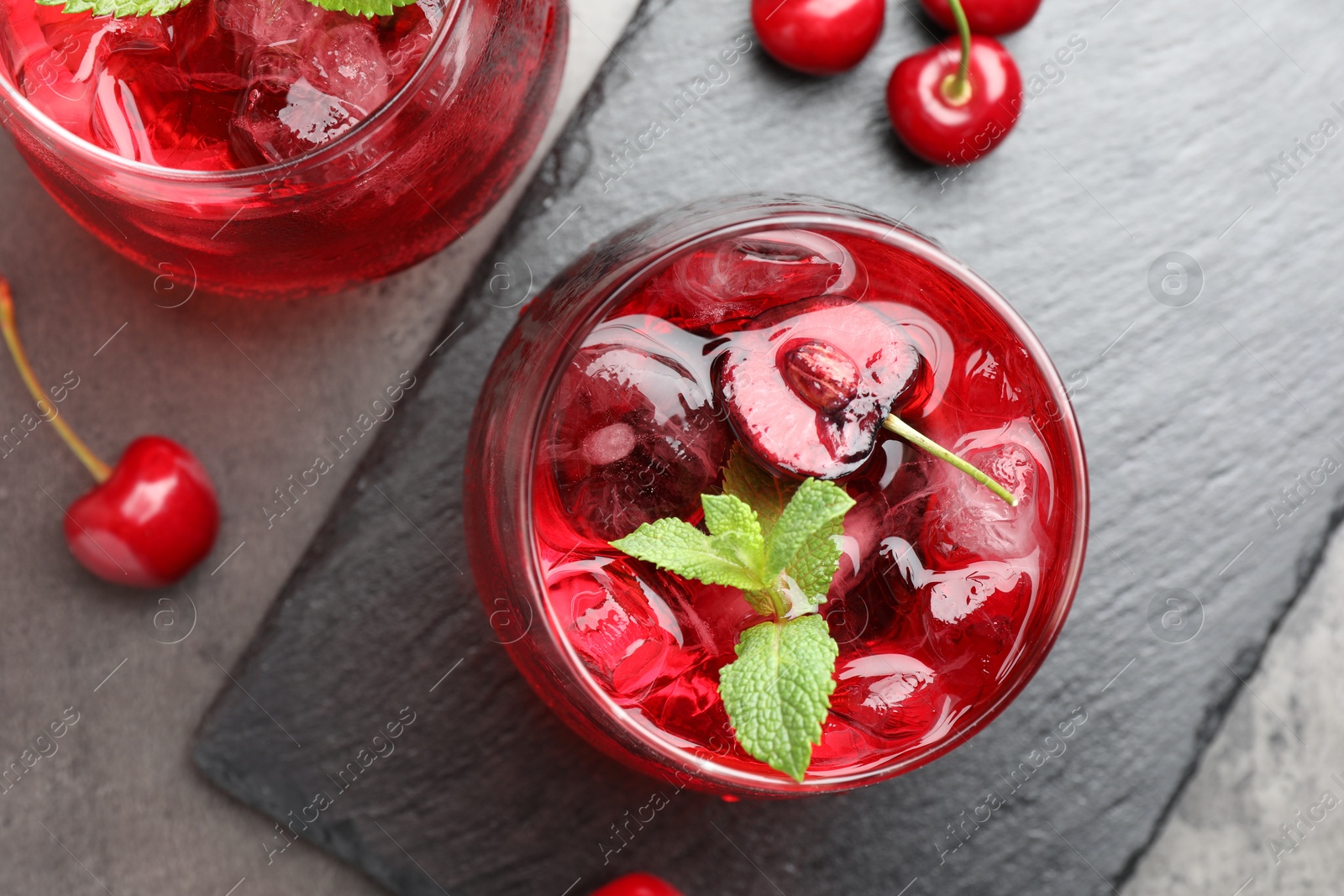 Tasty cherry soda with ice cubes, berries and mint in glasses on grey table, flat lay Photo of Tasty cherry soda with ice cubes, berries and mint in glasses on grey table, flat lay