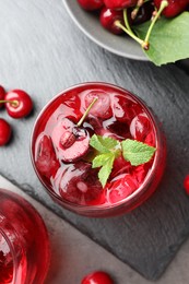 Photo of Tasty cherry soda with ice cubes, berries and mint in glasses on grey table, flat lay